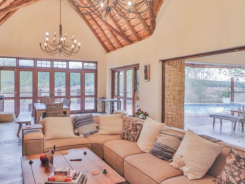 Spacious open-plan living area featuring high vaulted thatched ceilings with exposed timber trusses, stone accents, and seamless flow to an outdoor patio and pool.