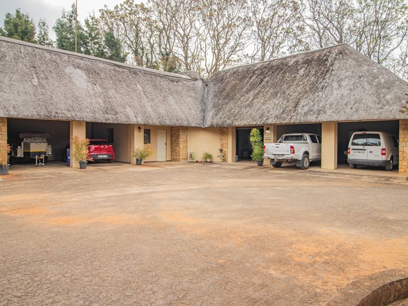 Spacious multi-bay garage area featuring traditional thatched roofing and stone-clad pillars, set against a large paved driveway on a small holding property.