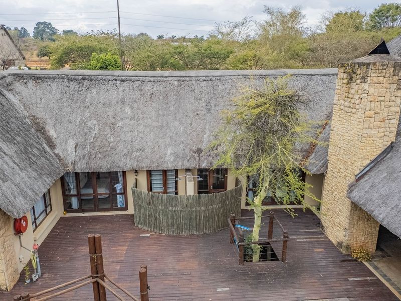 An elevated view of a spacious timber deck patio featuring a thatched roof, stone chimney, and an integrated outdoor shower area.