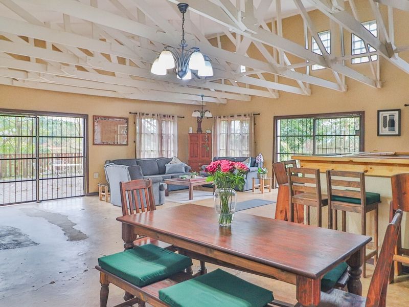 Spacious open-plan living and dining area featuring high vaulted ceilings with exposed timber trusses, tiled flooring, and direct access to the patio.