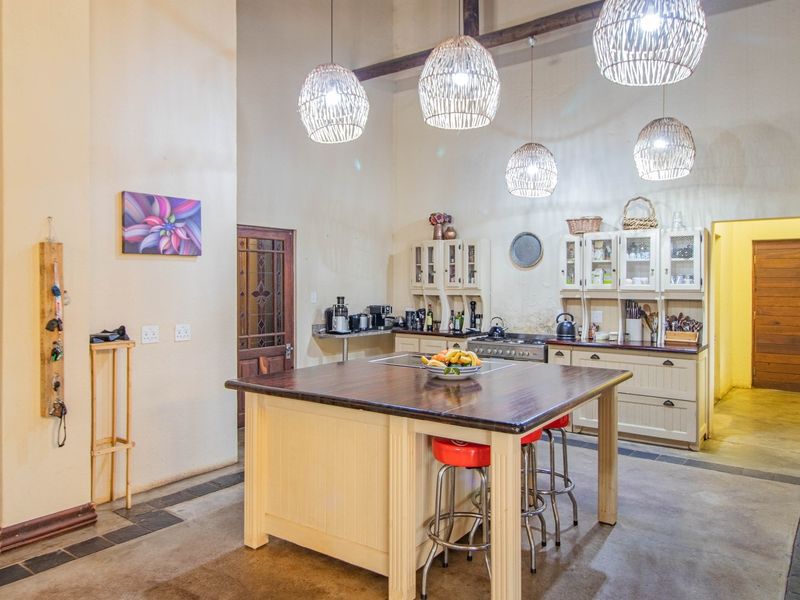 Spacious farmhouse-style kitchen featuring a large central island, built-in cabinetry, exposed timber beams, and high ceilings with pendant lighting.