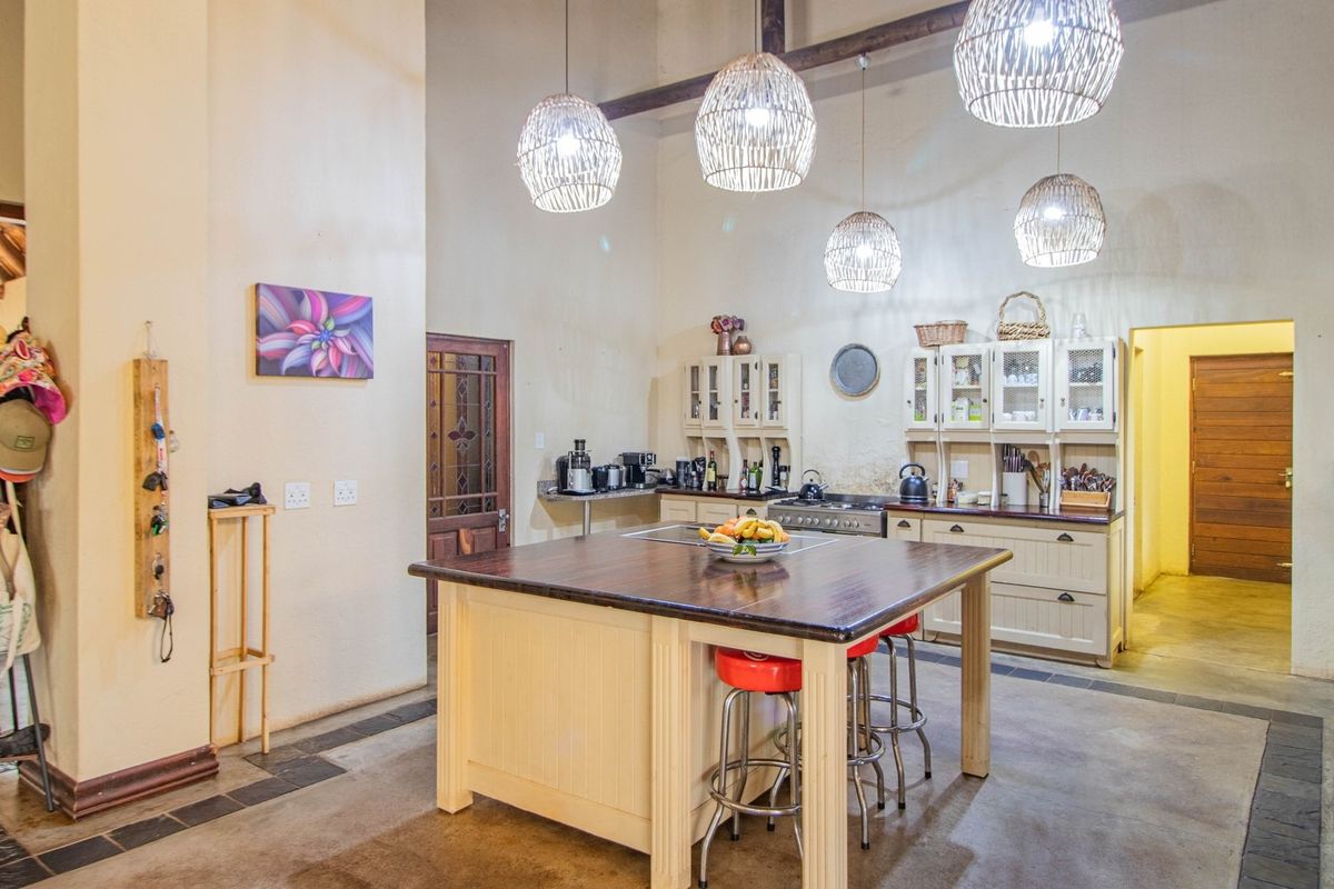 Spacious farmhouse-style kitchen featuring a large central island, built-in cabinetry, exposed timber beams, and high ceilings with pendant lighting.