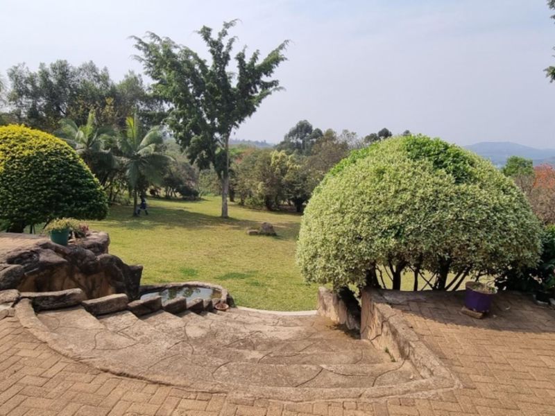 A spacious garden area featuring a paved patio, stone steps, and a retaining wall overlooking a well-maintained lawn and mature trees.