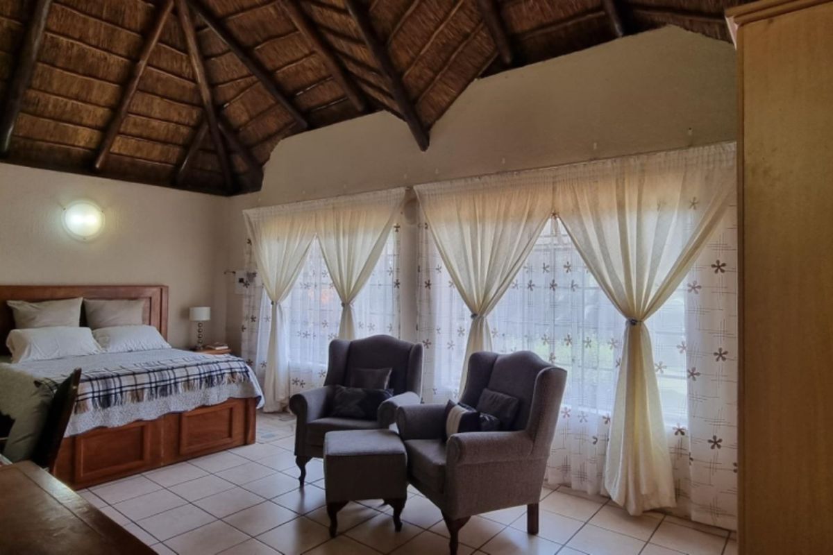Spacious bedroom featuring a high vaulted thatched ceiling with exposed timber rafters and large windows allowing for ample natural light.