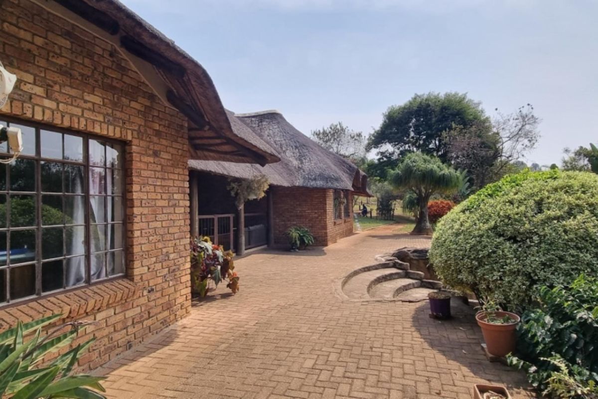 A rear view of a face brick small holding dwelling featuring a traditional thatched roof and an expansive paved patio area.