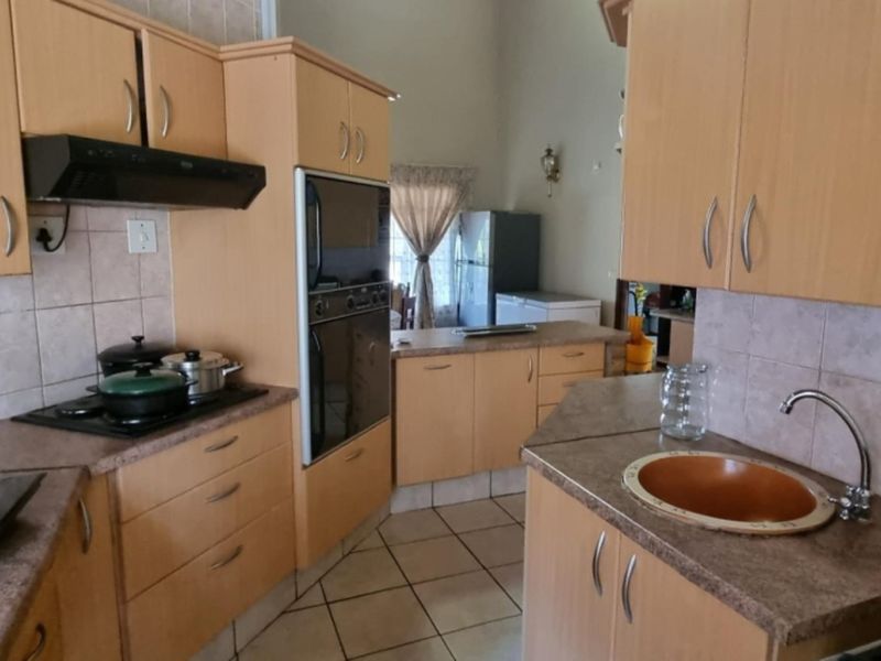 Functional kitchen featuring light wood-tone cabinetry, laminate countertops, built-in oven, extractor fan, and tiled backsplash with neutral floor tiles.