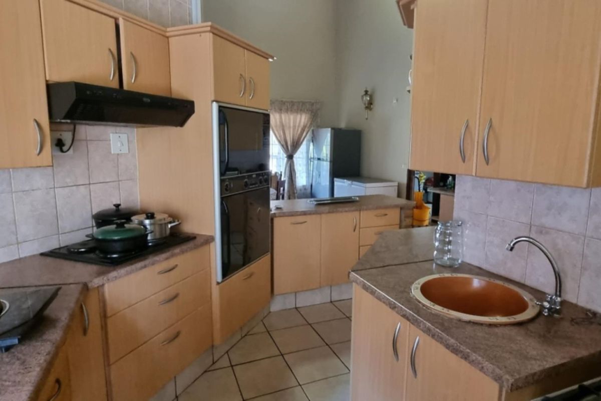 Functional kitchen featuring light wood-tone cabinetry, laminate countertops, built-in oven, extractor fan, and tiled backsplash with neutral floor tiles.