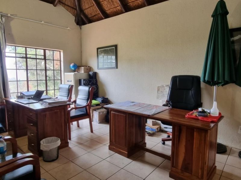 A spacious home office featuring a high thatched ceiling with exposed rafters, tiled flooring, and large windows providing natural light.