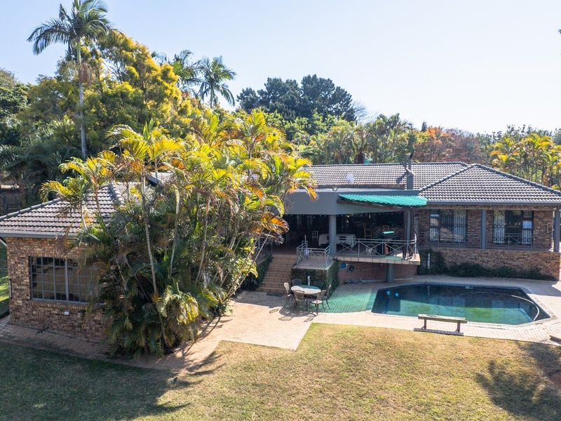Aerial view of the rear exterior featuring a brick-faced dwelling, a swimming pool, and a covered patio area set within a landscaped garden.