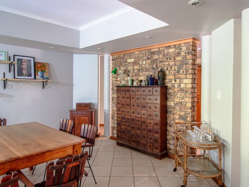 Dining area featuring an exposed brick feature wall, recessed ceiling with downlights, and neutral ceramic floor tiles.