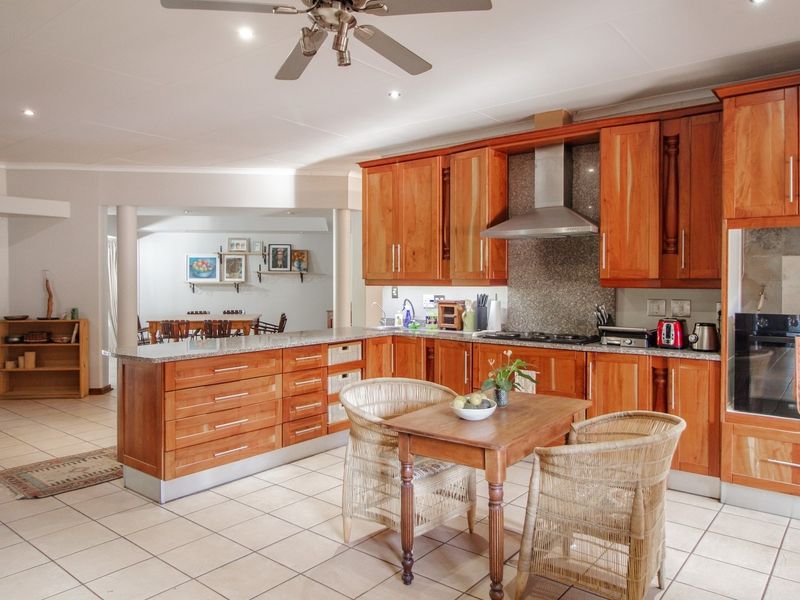 Spacious open-plan kitchen featuring warm wooden cabinetry, granite countertops, and integrated appliances, flowing seamlessly into the adjacent dining area.