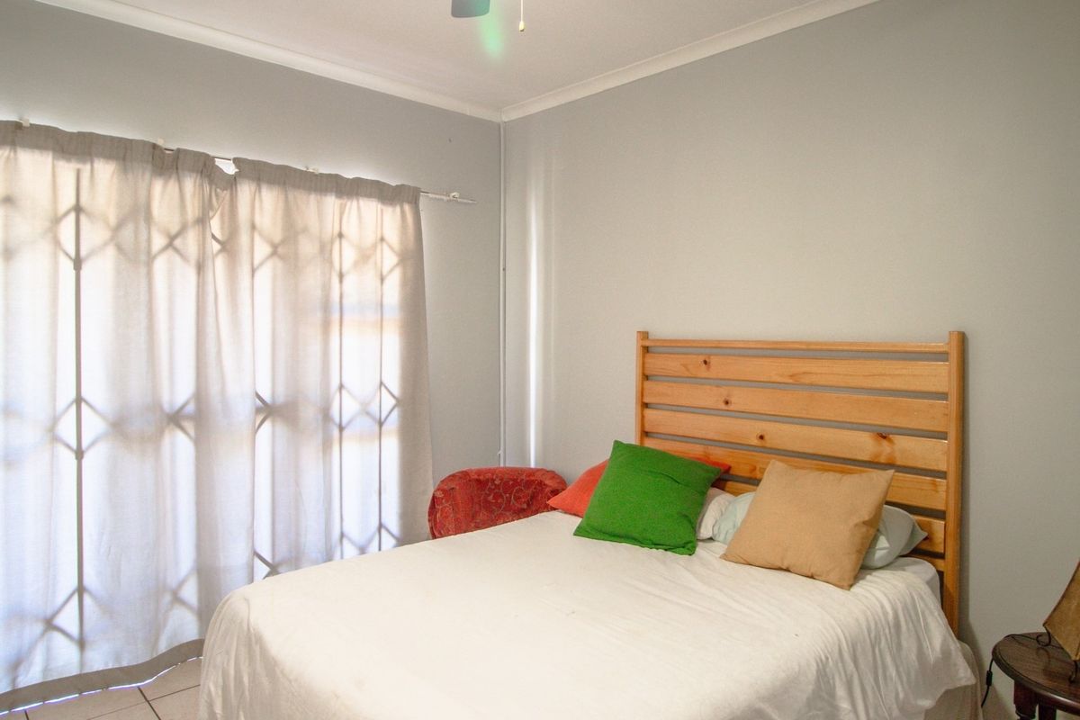 A functional bedroom featuring tiled flooring, a ceiling fan, and a security gate over the window for added peace of mind.