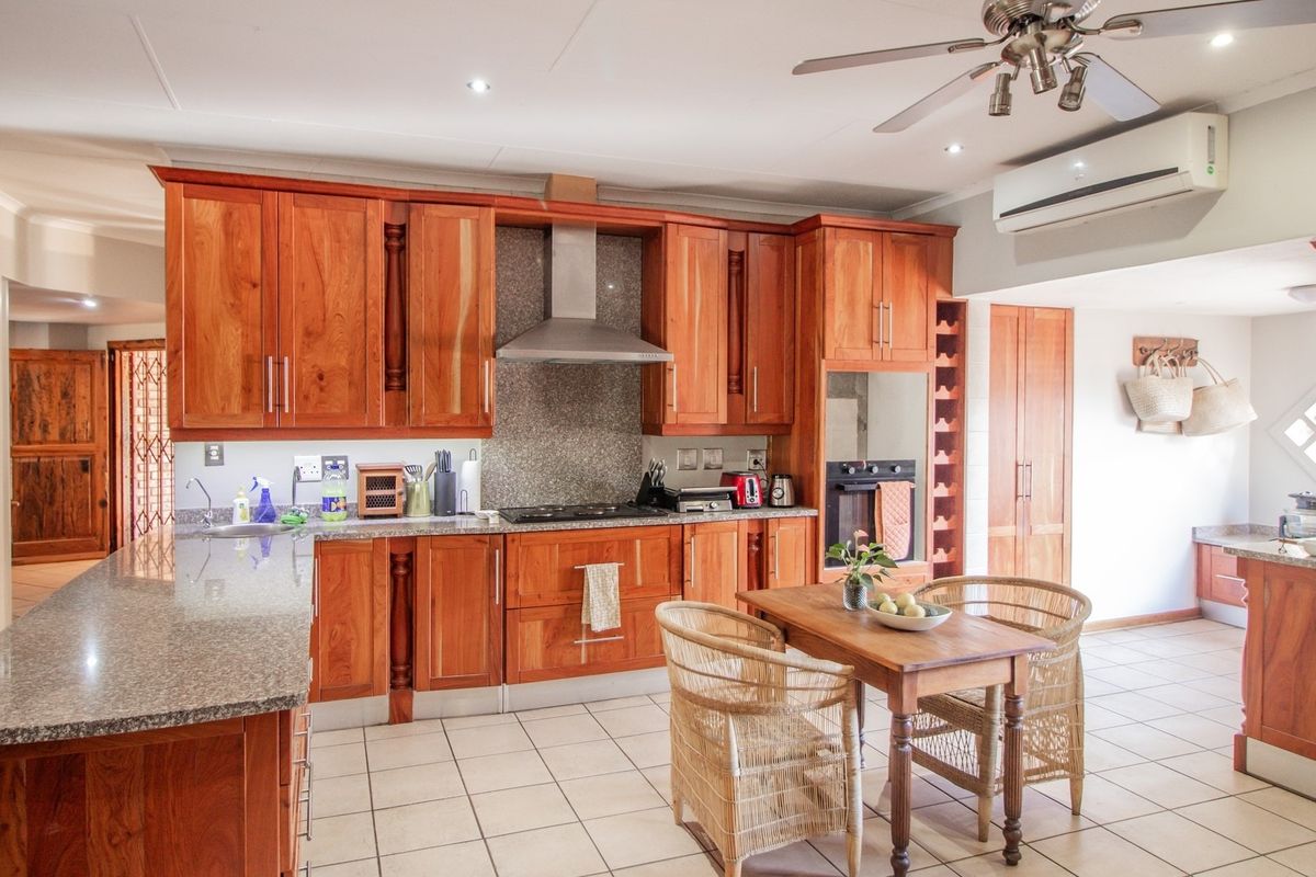 Spacious kitchen featuring warm wooden cabinetry, granite countertops, built-in oven, gas hob, and an integrated wine rack, complemented by tiled flooring and air conditioning.