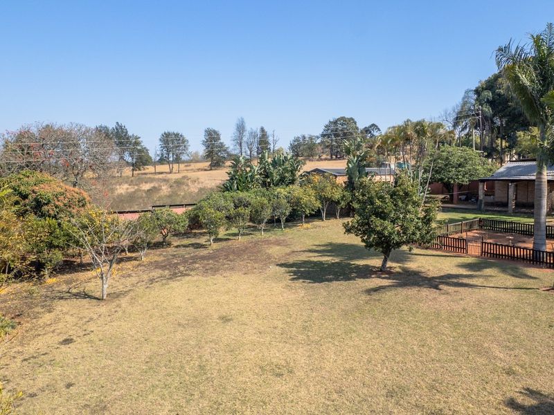 Spacious garden area featuring mature trees, a fenced enclosure, and expansive lawn space on a small holding property.