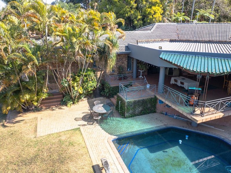 Elevated view of a backyard featuring a swimming pool, paved patio area, and a raised covered veranda with metal railings.
