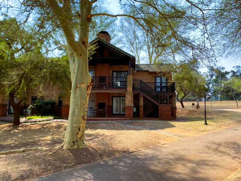 Rear view of a double-story brick house featuring a balcony, external staircase, and a built-in braai area set within a landscaped garden.