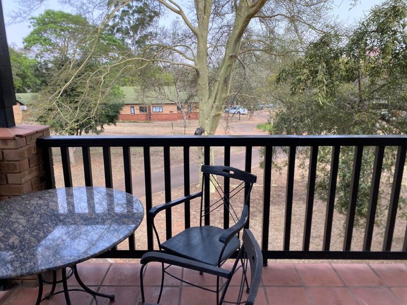 A covered balcony featuring tiled flooring and a protective railing, offering an elevated view of the surrounding garden and neighborhood.