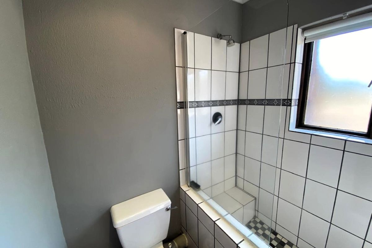 A functional bathroom featuring a shower with a glass screen, tiled surround, and a standard toilet.