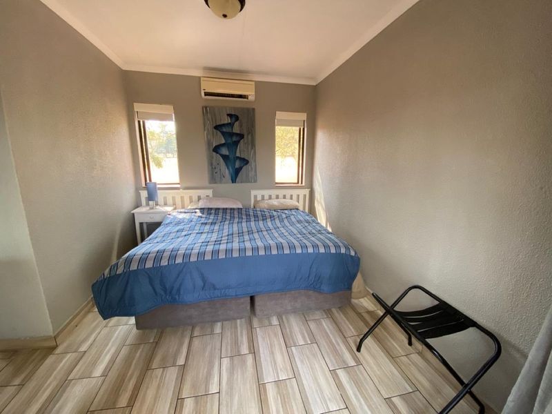 A well-maintained bedroom featuring modern tiled flooring, neutral wall finishes, and a wall-mounted split-system air conditioning unit.
