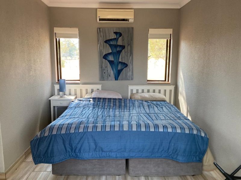 A well-maintained bedroom featuring tiled flooring, dual windows with roller blinds, and a wall-mounted split-system air conditioning unit.