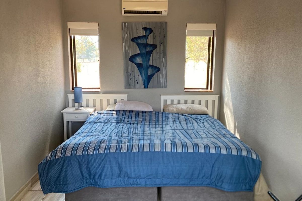 A well-maintained bedroom featuring tiled flooring, dual windows with roller blinds, and a wall-mounted split-system air conditioning unit.
