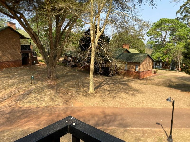 An elevated view overlooking a landscaped garden area with brick buildings, mature trees, and paved pathways.