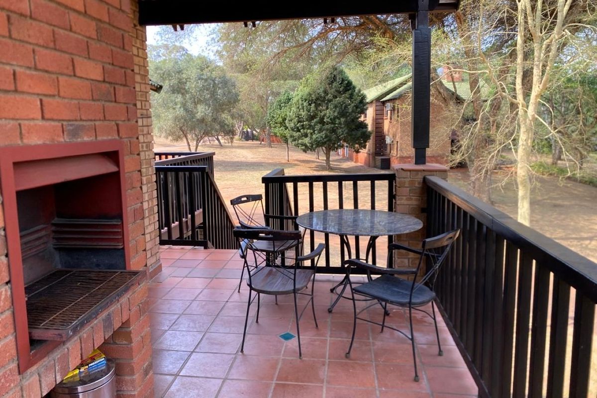 Covered balcony featuring a built-in brick braai, tiled flooring, and a timber balustrade overlooking the surrounding garden area.