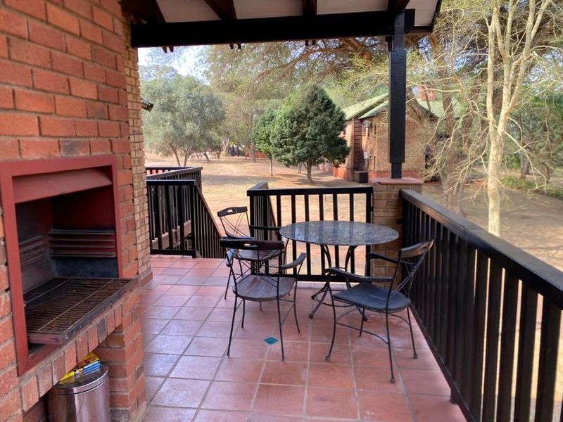 Covered balcony featuring a built-in brick braai, tiled flooring, and a timber balustrade overlooking the surrounding garden area.