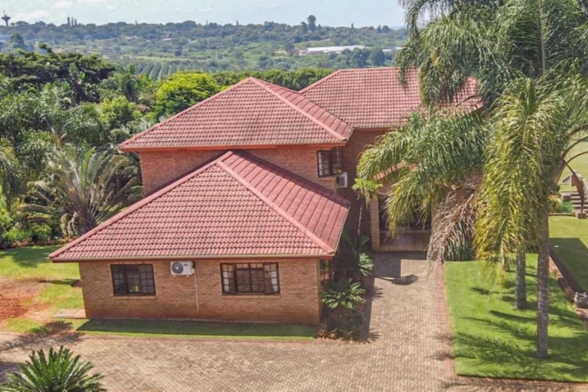 Aerial view of a brick-faced house with a tiled roof, featuring a paved driveway and established garden surroundings.