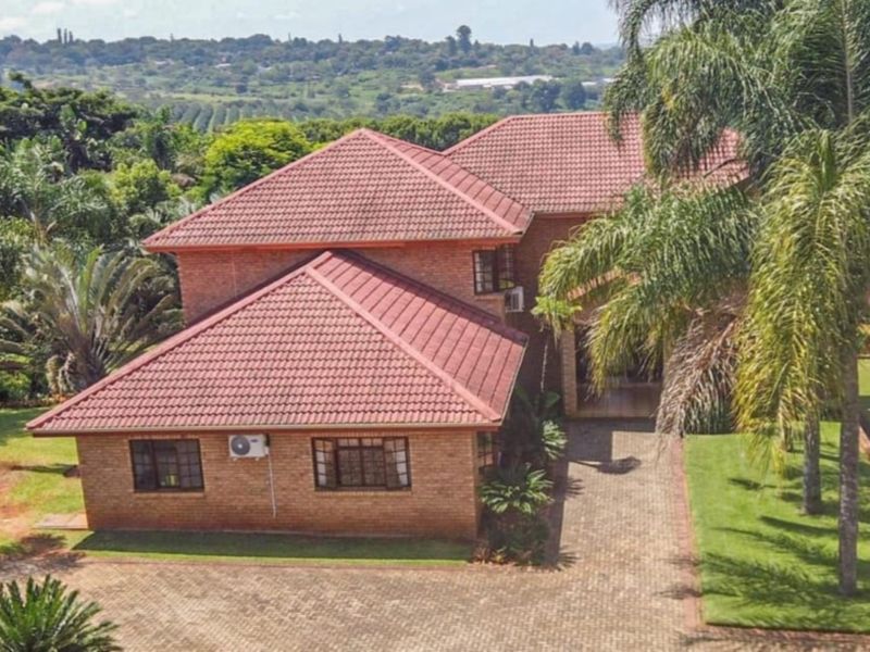 Aerial view of a brick-faced house with a tiled roof, featuring a paved driveway and established garden surroundings.