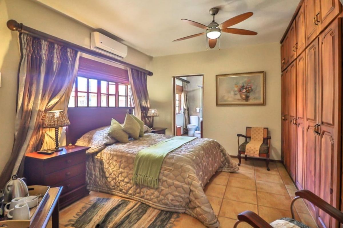 A spacious bedroom featuring built-in wooden cupboards, tiled flooring, a ceiling fan, and an integrated air conditioning unit, with an en-suite bathroom visible.