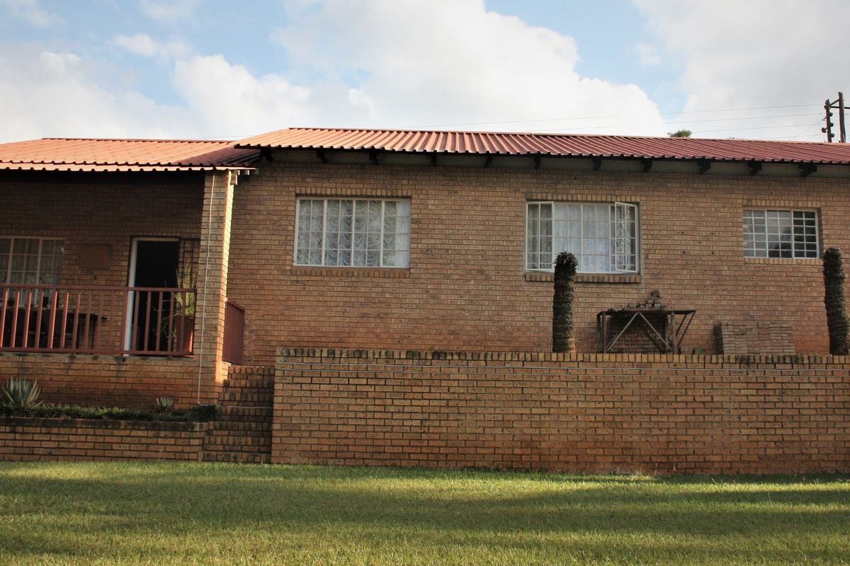 Rear view of a face brick house featuring a corrugated metal roof, a covered patio area, and a brick retaining wall overlooking the garden.