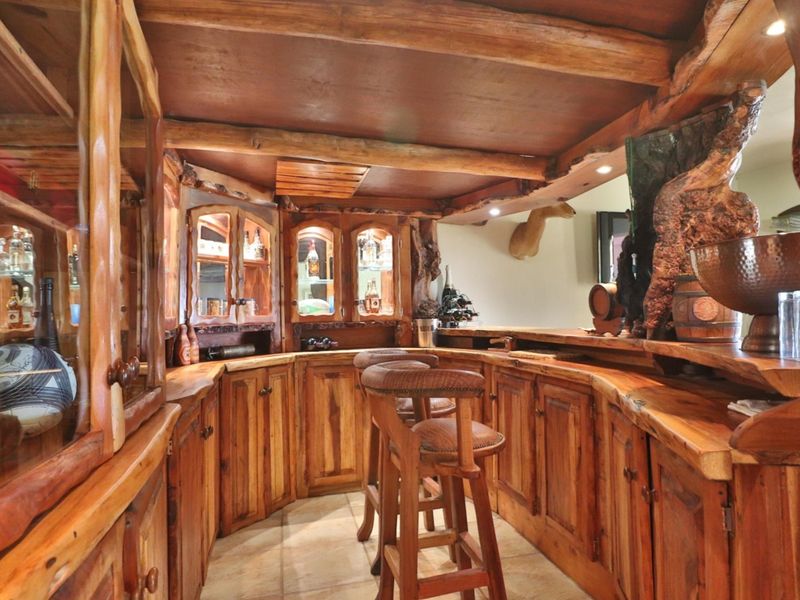 A rustic custom-built home bar featuring extensive live-edge timber cabinetry, integrated display lighting, and a solid wood bar counter.