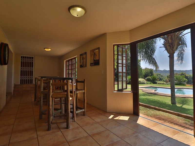 Covered patio area featuring tiled flooring and direct access to the garden and swimming pool area through large casement doors.