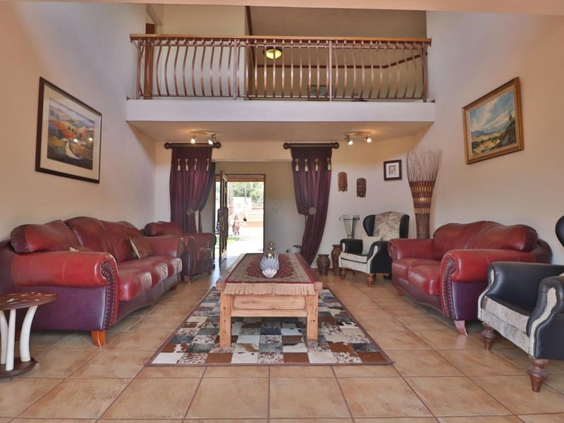 Spacious double-volume living room featuring tiled flooring, a mezzanine level with a metal balustrade, and direct access to the exterior entrance.