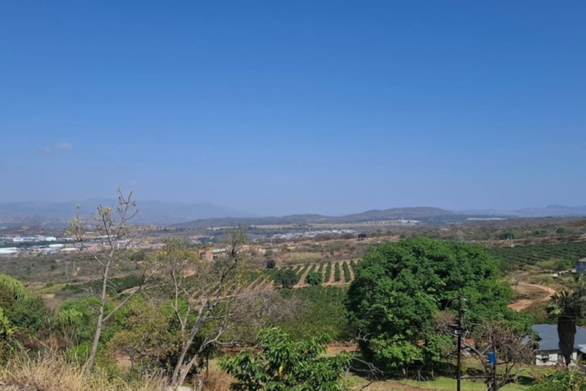 A wide-angle view overlooking a rural landscape with rolling hills, agricultural fields, and distant residential development under a clear blue sky.