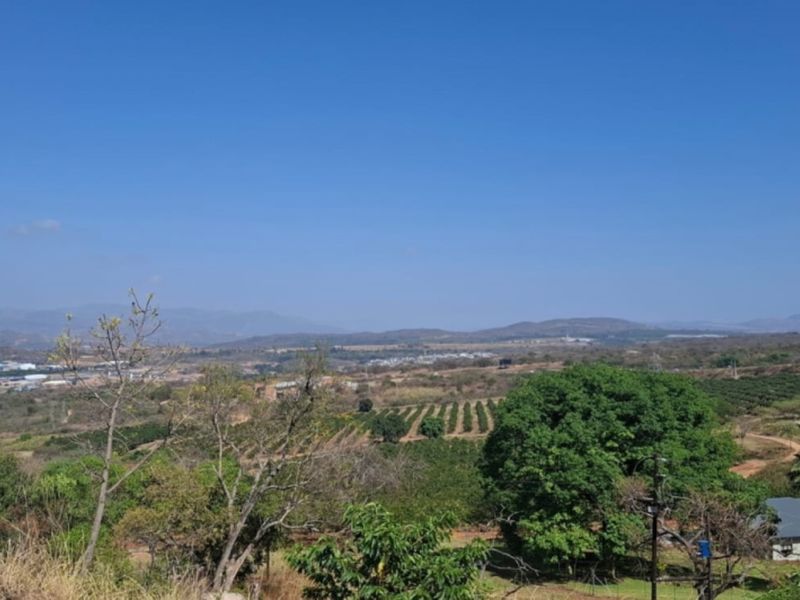 A wide-angle view overlooking a rural landscape with rolling hills, agricultural fields, and distant residential development under a clear blue sky.