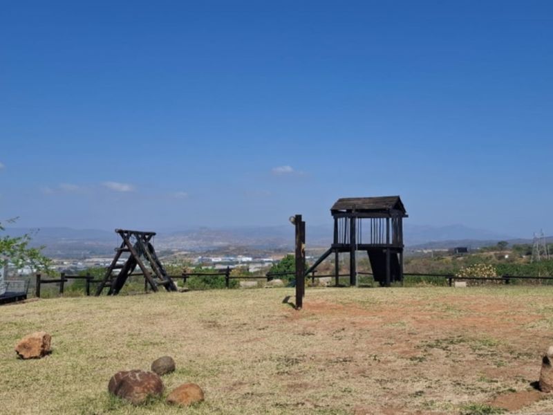Expansive elevated view overlooking the surrounding landscape, featuring a grassy area with a wooden play structure and perimeter fencing.