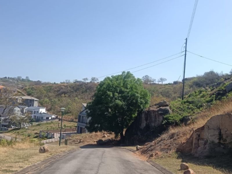 A view of the paved access road leading through the residential estate, featuring natural rocky terrain and surrounding hillside landscape.