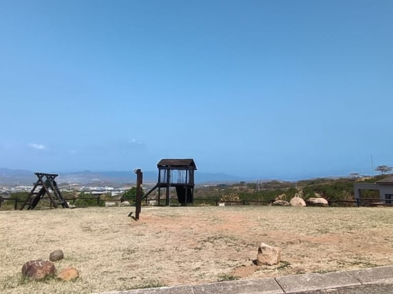 An open residential plot featuring dry grass, timber fencing, and existing playground structures with distant landscape views.