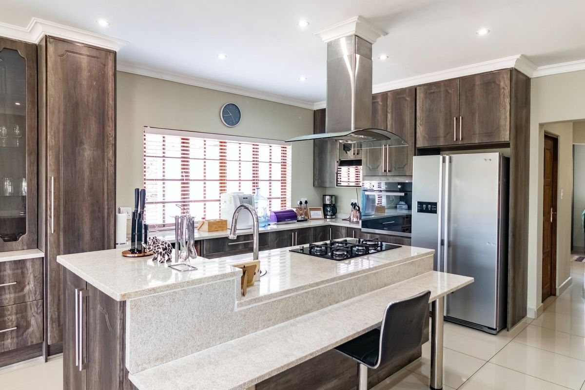 Modern kitchen featuring dark wood cabinetry, stone countertops, a central island with a gas hob, and integrated stainless steel appliances.