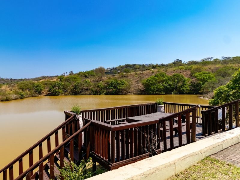 Elevated timber deck patio overlooking a natural dam, featuring wooden balustrades and stairs with direct access to the surrounding landscape.