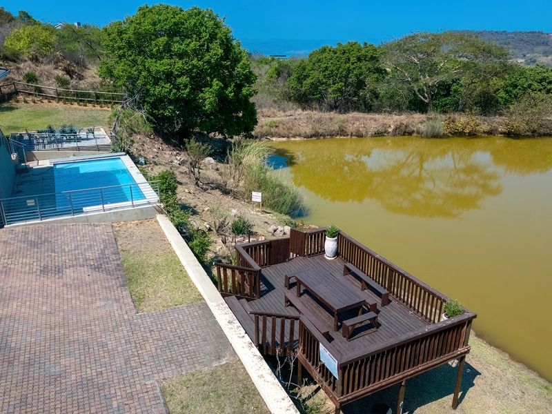 Aerial view of a property featuring a swimming pool, paved driveway, and a wooden deck overlooking a large pond.