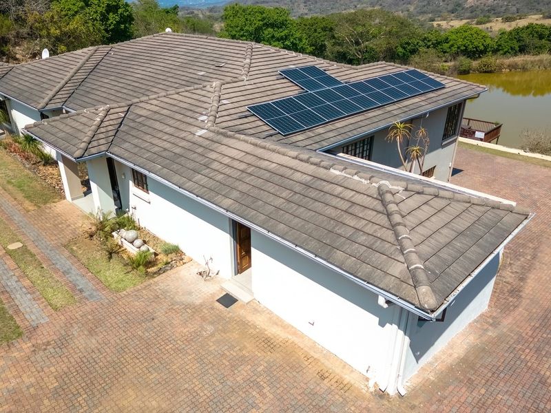 Aerial view of the property featuring a tiled roof with installed solar panels, a paved driveway, and surrounding landscaped grounds near a pond.