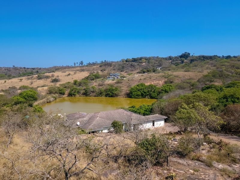 Aerial view of a residential property situated in a rural landscape, featuring a tiled roof house adjacent to a natural pond.