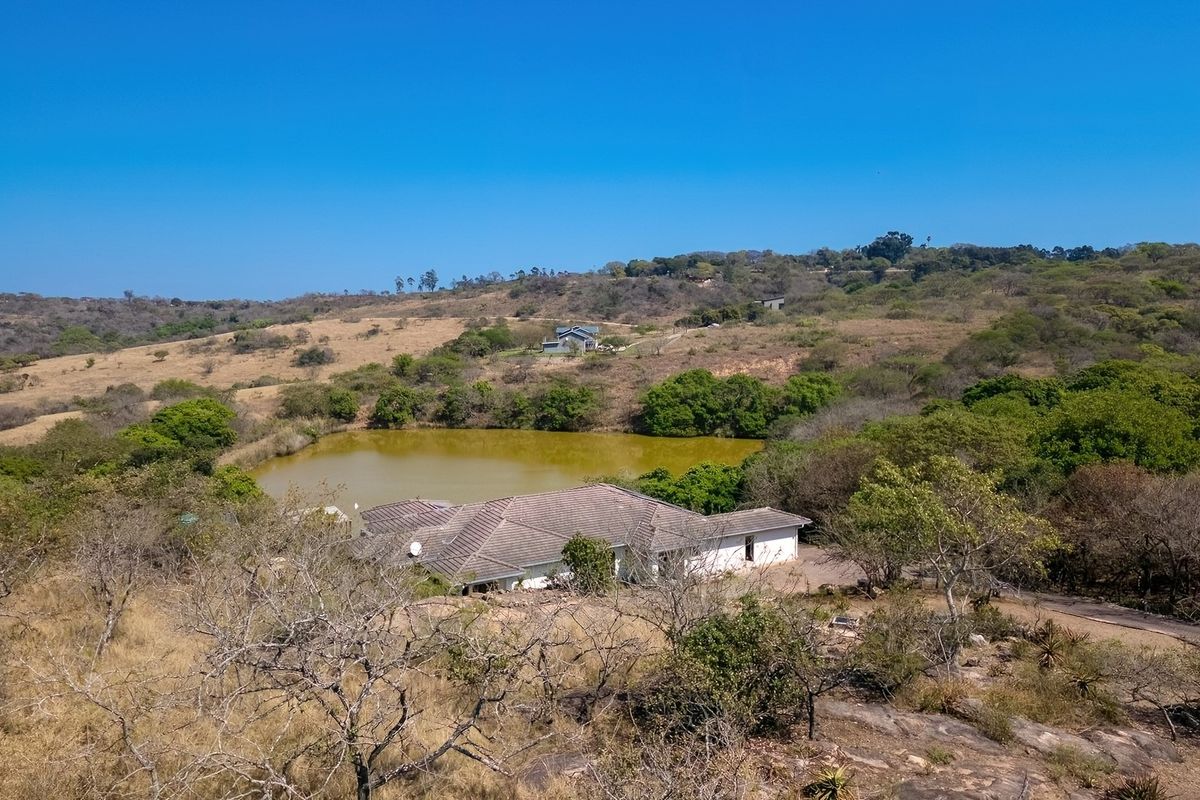 Aerial view of a residential property situated in a rural landscape, featuring a tiled roof house adjacent to a natural pond.