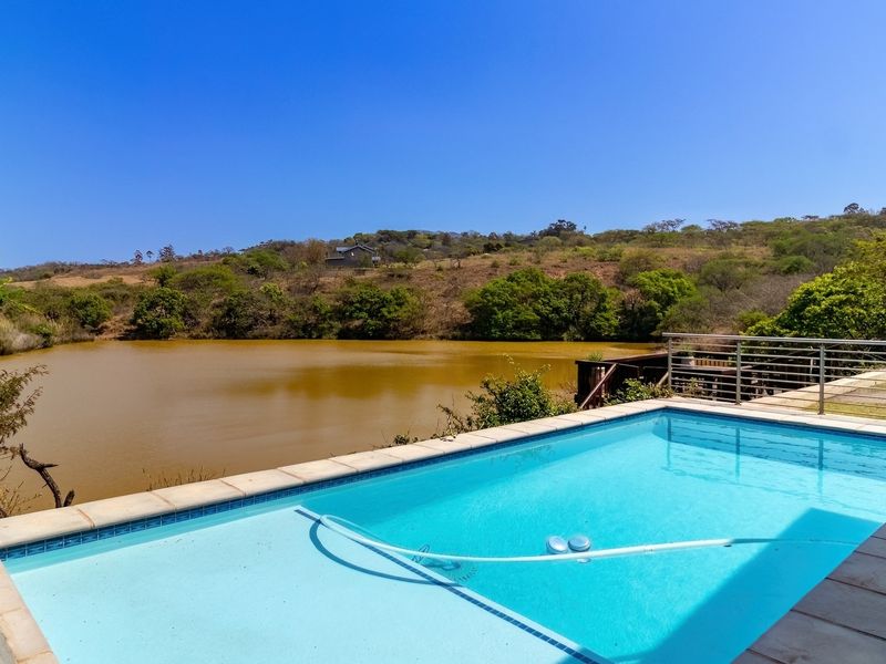 A well-maintained swimming pool with a tiled surround, featuring a scenic view of the surrounding landscape and a nearby dam.