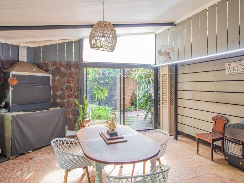 Covered patio area featuring a built-in braai, tiled flooring, and sliding glass doors opening to a private garden space.