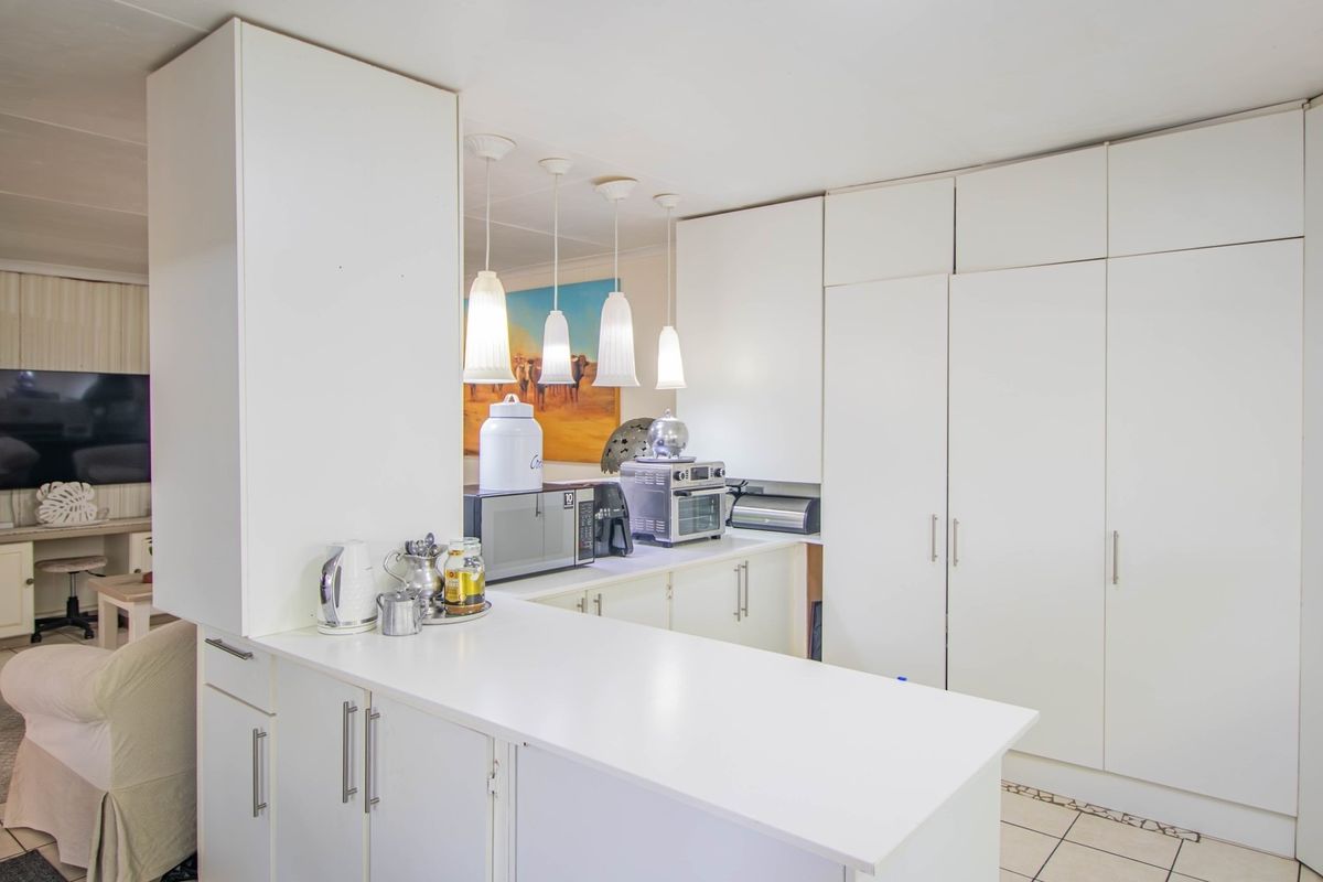A functional kitchen featuring white built-in cabinetry, laminate countertops, and pendant lighting, seamlessly flowing into the adjacent living area.