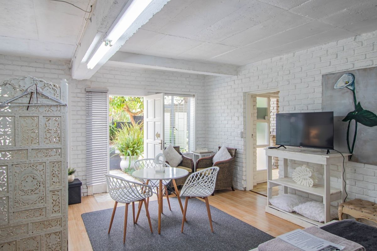 A living area featuring painted brick walls, exposed beam ceilings, laminate flooring, and direct access to an outdoor patio through french doors.